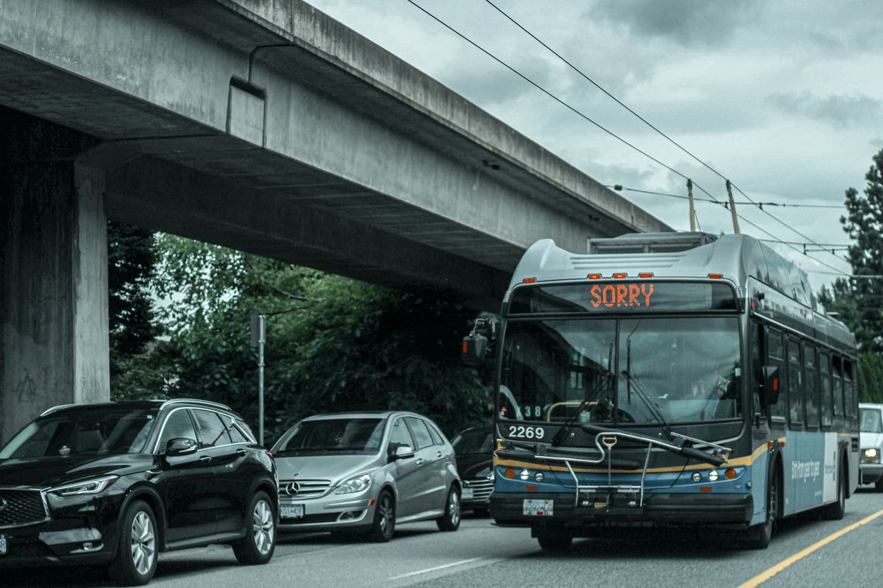 A busy city street with traffic and a bus showing 'SORRY' on its display under an overpass.